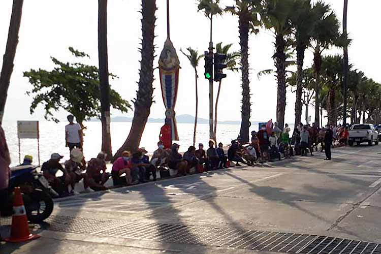 Thaier sitter i kø i påvente av en matutdeling på Jomtien Beach. Selve stranda er helt tom.